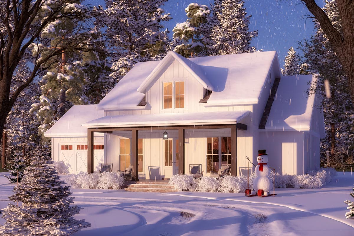 A snow-covered white house during winter with a snowman and trees in the background. Snow blankets the roof, yard and surrounding woods.