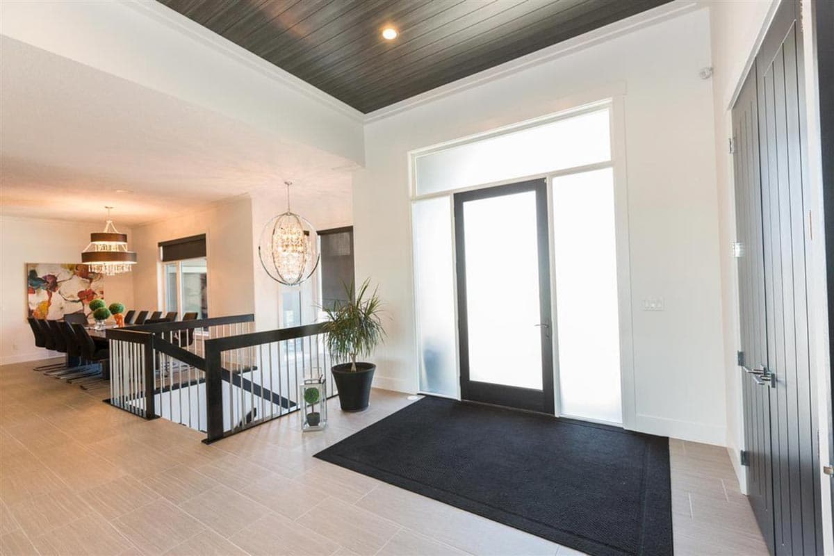 Modern entryway with frosted glass door, dark wood planks, tiered chandelier, and a dining area visible.