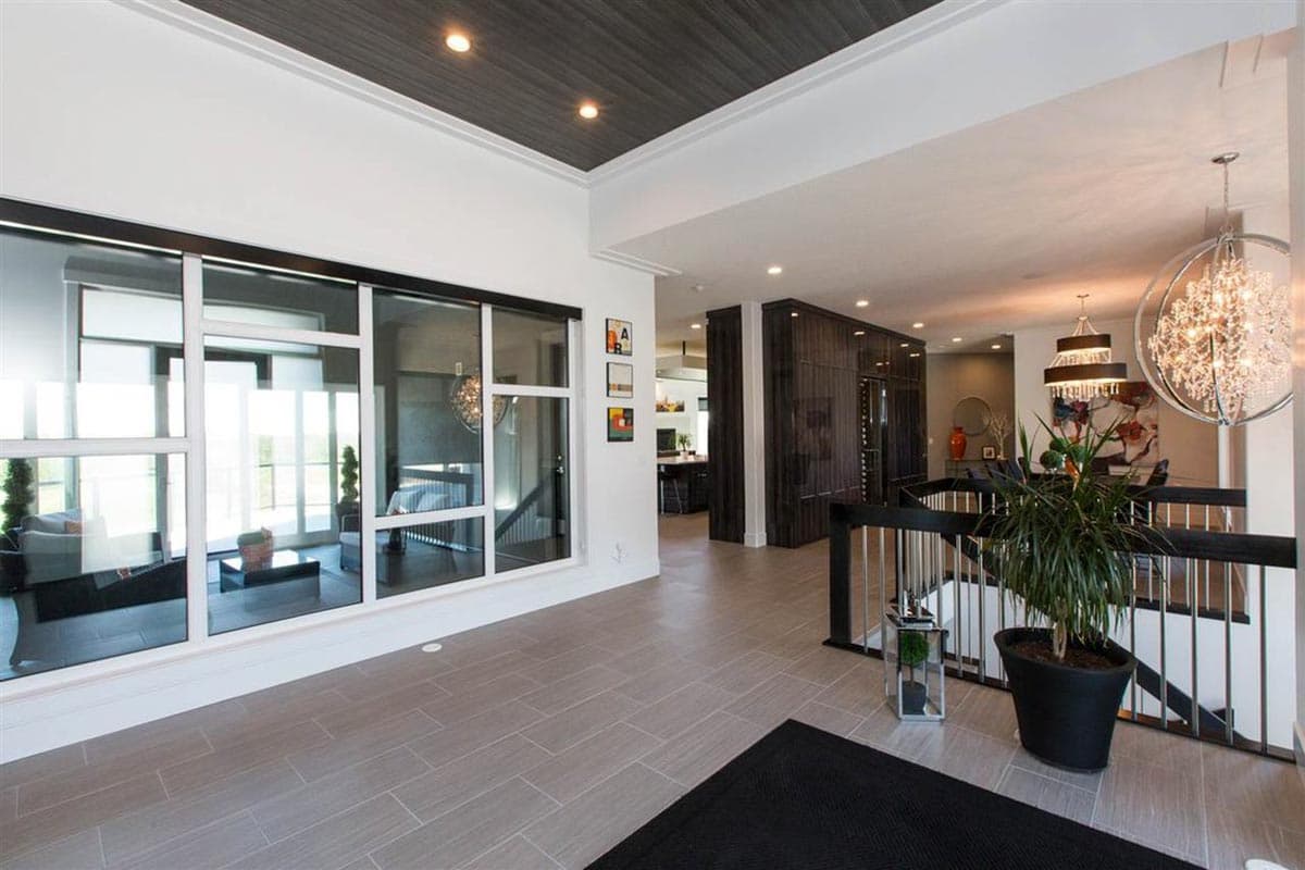 Interior view of a modern home entry with large windows, wood-paneled ceiling, dark wood cabinetry, and a grand staircase.