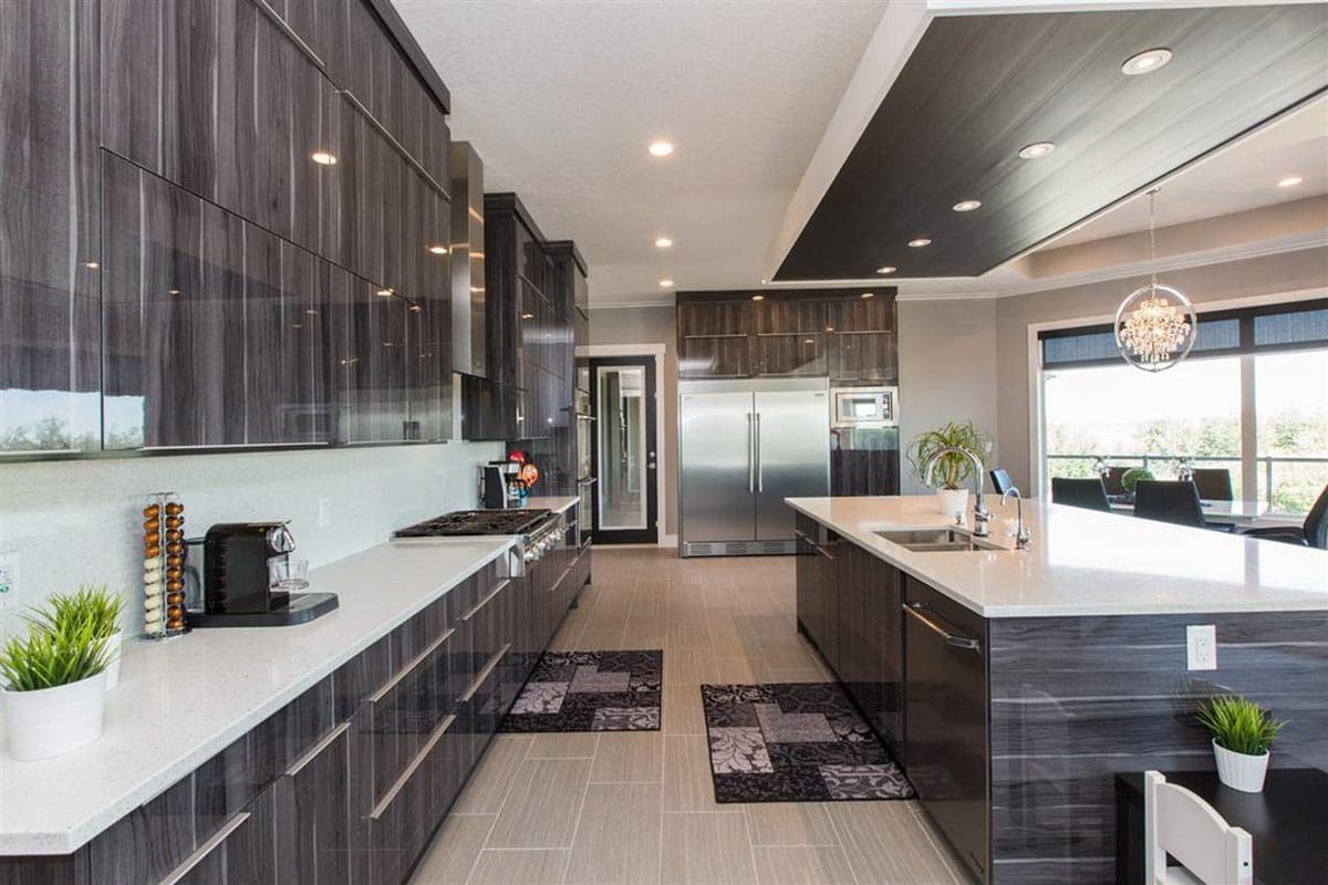 Modern kitchen with dark wood cabinetry, large island with sink, stainless steel appliances, and pendant lighting.
