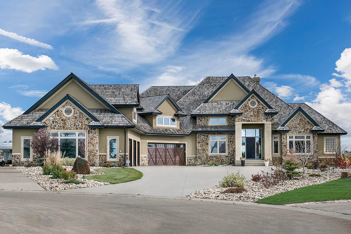 House plan exterior. Two-story, with stone accents and a cedar shake roof. Features include gables, dormers, and a three-car garage.