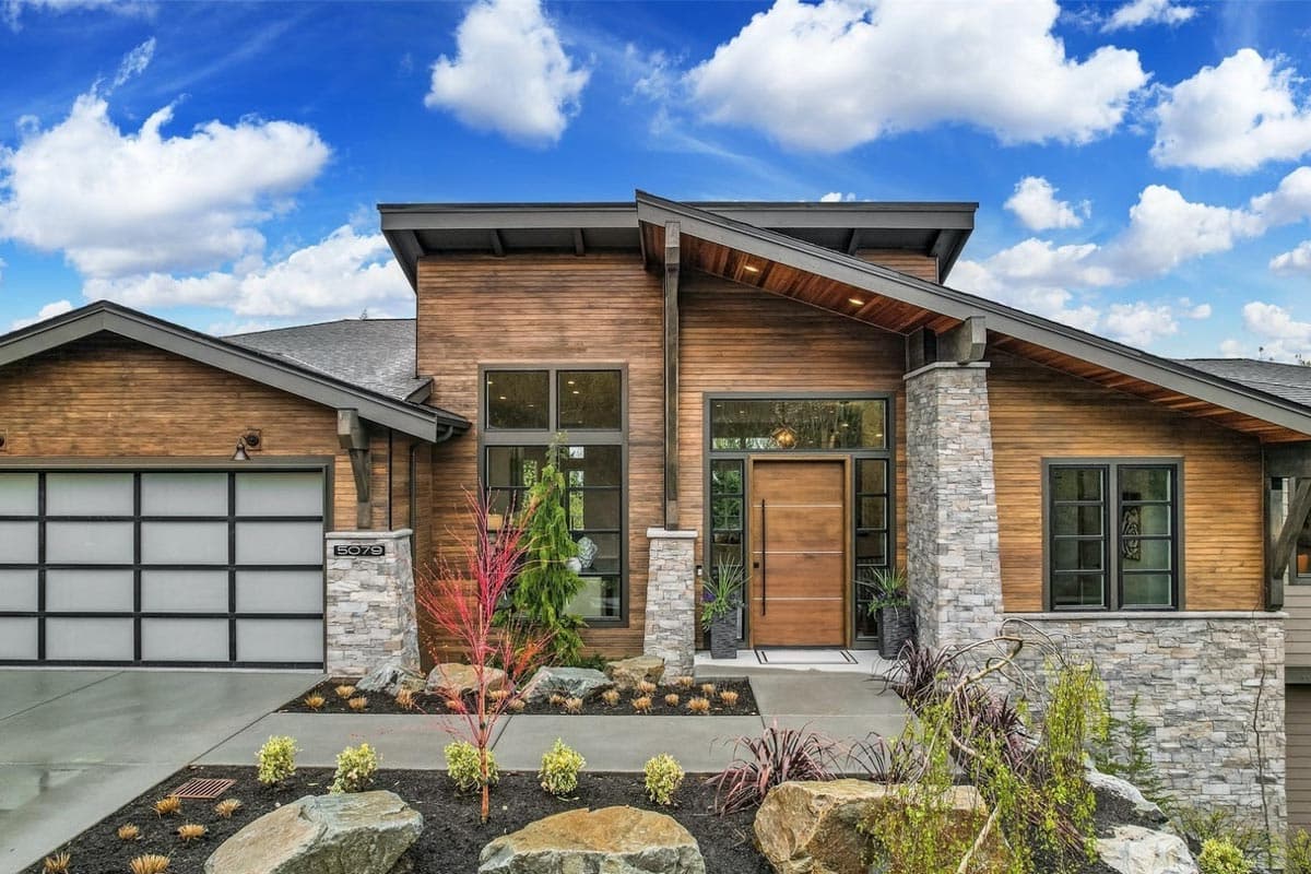 House plan exterior. Modern style with wood siding, stone accents, and a sloped roof. Features include an attached garage and large windows.