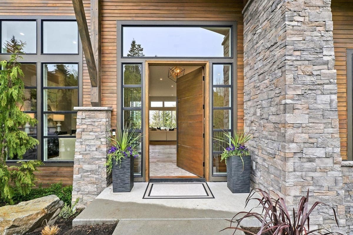 Modern house exterior with wood siding, stone accents, large windows, and a double wooden pivot door.