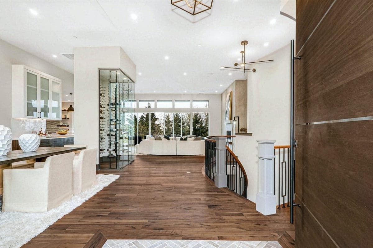 Interior view showcasing a modern great room with a large sectional, floor-to-ceiling windows, and a glass wine cellar.