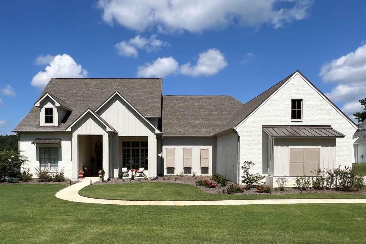 House plan exterior featuring a two-story design with a gable roof, a covered porch, and dormers. The home has a brick and wood exterior.