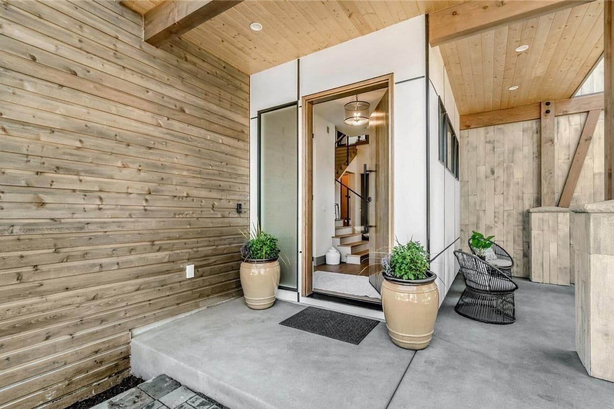 Modern house exterior with wood siding, open entryway, and visible staircase leading upstairs.