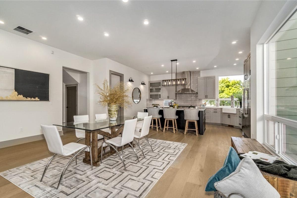 Open concept dining area and kitchen with island, pendant lights, range hood, gray cabinetry, and large windows.