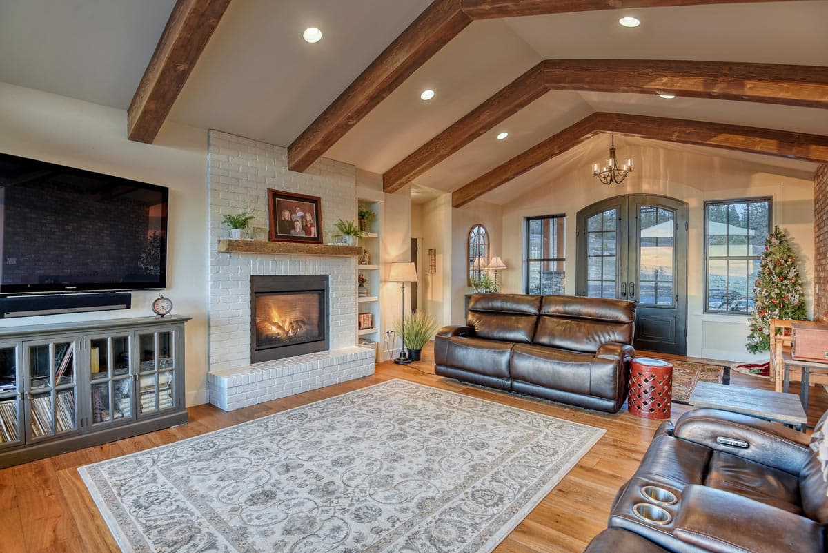 Interior view of a great room with vaulted ceiling, exposed wood beams, brick fireplace, and leather seating.