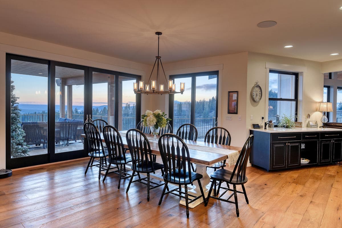 Dining room with long table, chairs, and sliding glass doors opening to a deck with mountain views.