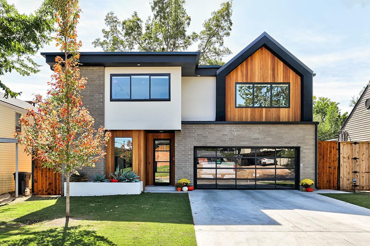 House plan exterior. Two-story modern house with a gable roof, wood cladding, and a glass-paneled garage door.