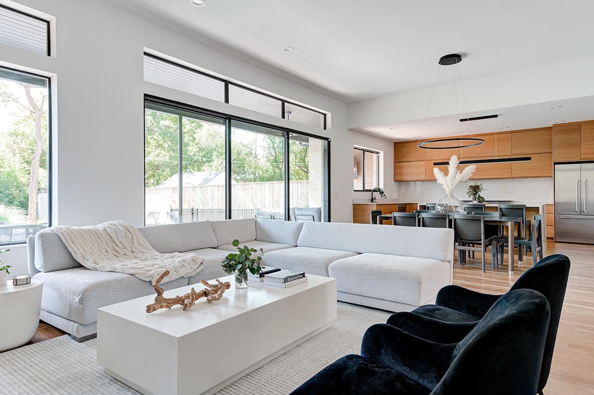 Open-concept living and dining area with sectional sofa, modern dining set, and kitchen with wood cabinetry.