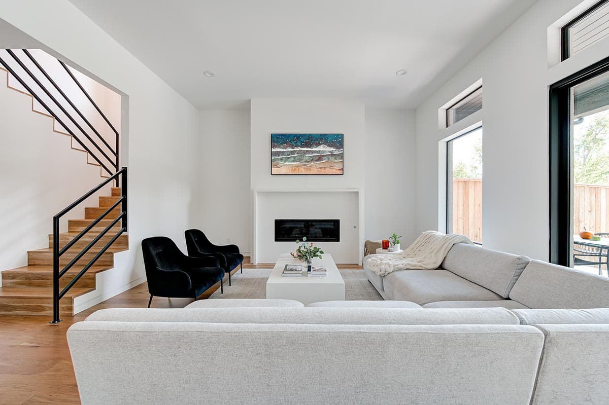 Modern living room with open staircase, fireplace, and large windows.