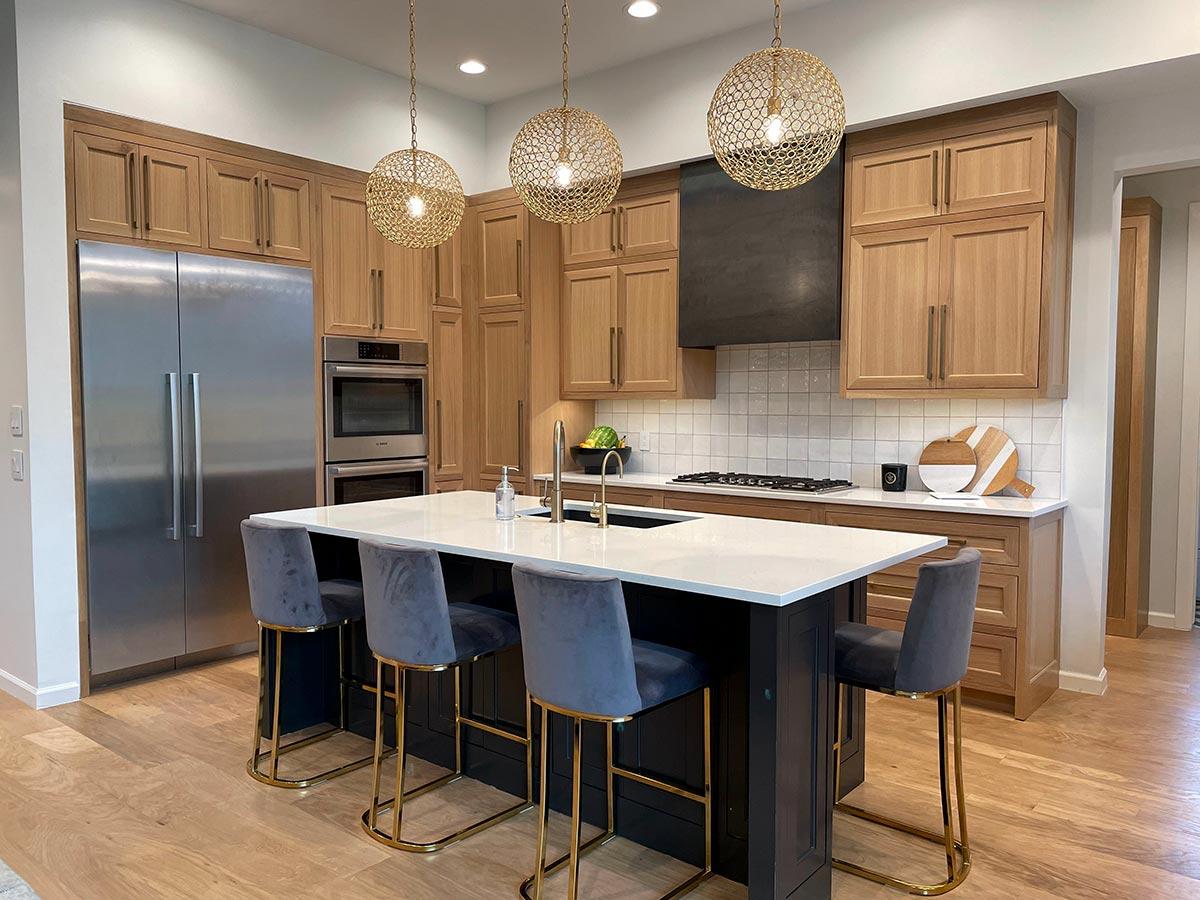 Modern kitchen with natural wood cabinetry, a large island with seating, stainless steel appliances, and three spherical pendant lights.