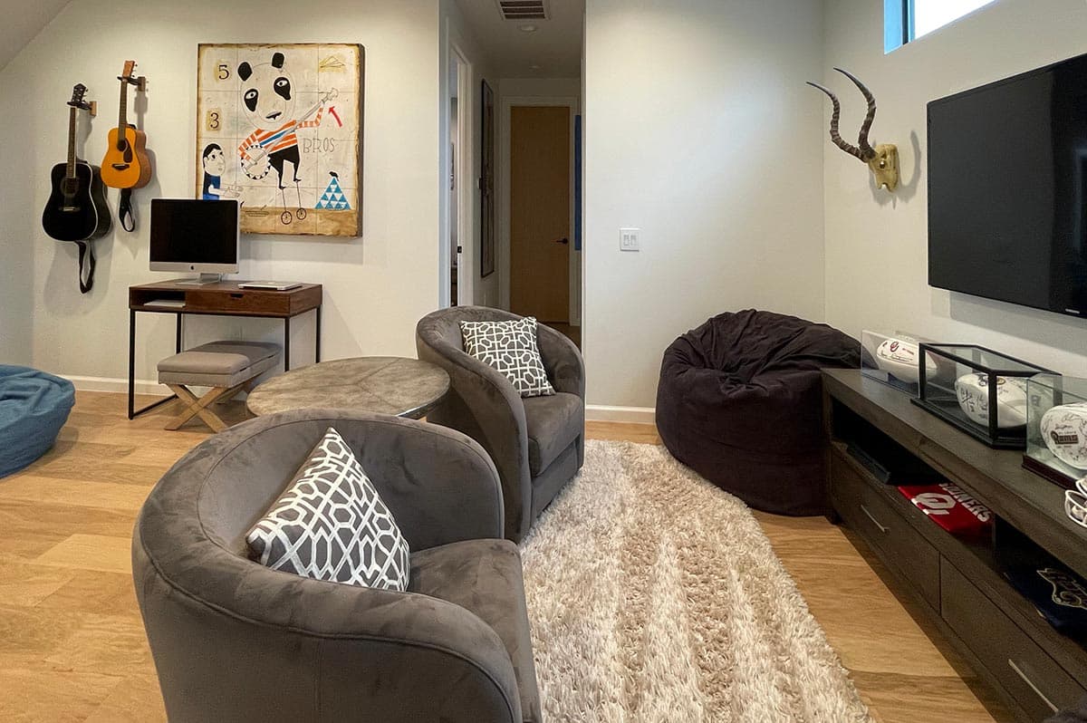 Living room with two gray armchairs, beanbag chairs, guitars on wall, desk, and television.