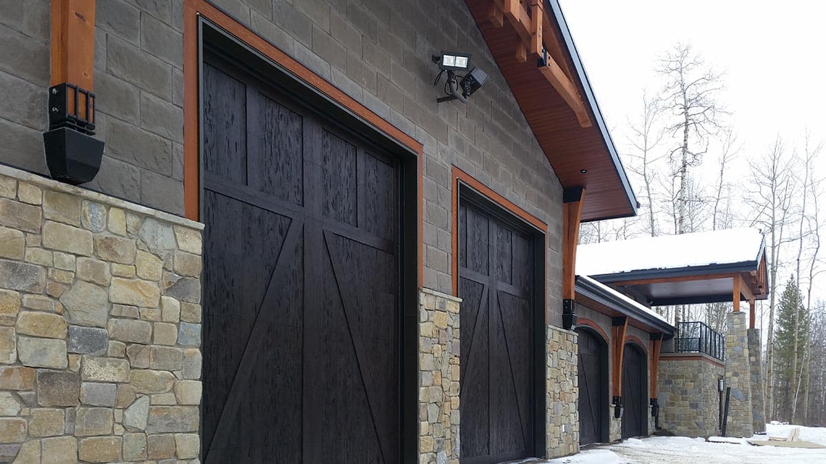 Exterior house plan with stone and grey brick facade, dark wood garage doors, and exposed wooden beams.