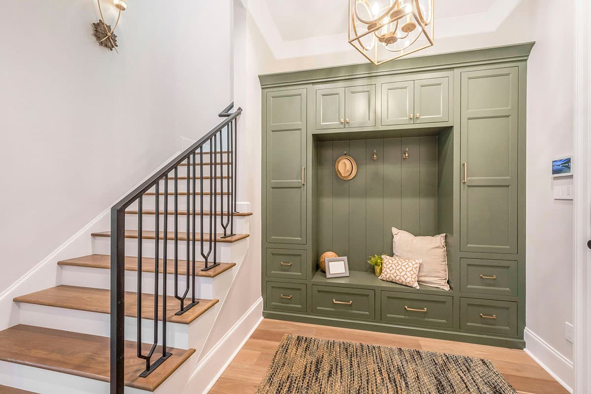 Entryway with built-in storage unit, bench seating, and staircase with black iron balustrade. Features include gold fixtures and light wood flooring.