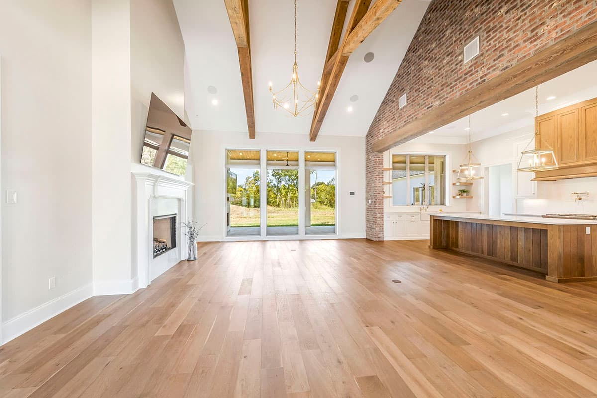 Interior rendering of a great room featuring a fireplace, exposed beams, and a brick accent wall with open-concept kitchen.