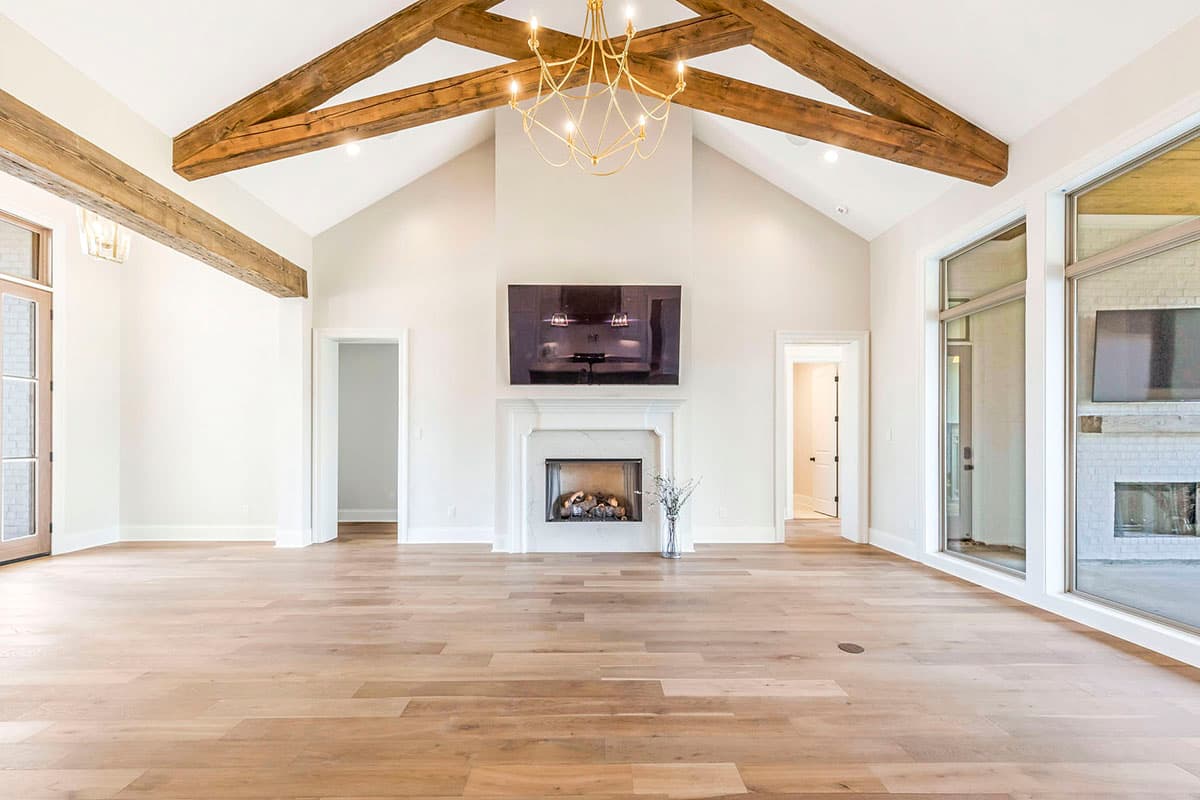 Great room with vaulted ceiling, exposed beams, fireplace, and large windows. Wood flooring and chandelier.