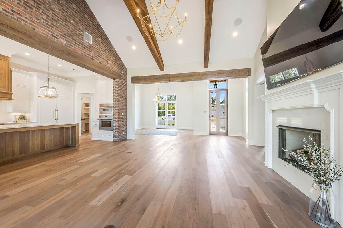 Interior view of great room with wood flooring, vaulted ceiling with exposed beams, brick accent wall, and fireplace with mantel.
