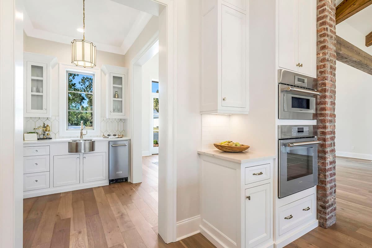 Kitchen interior with white cabinetry, stainless steel appliances, and a brick pillar. The room has hardwood flooring and a large window.