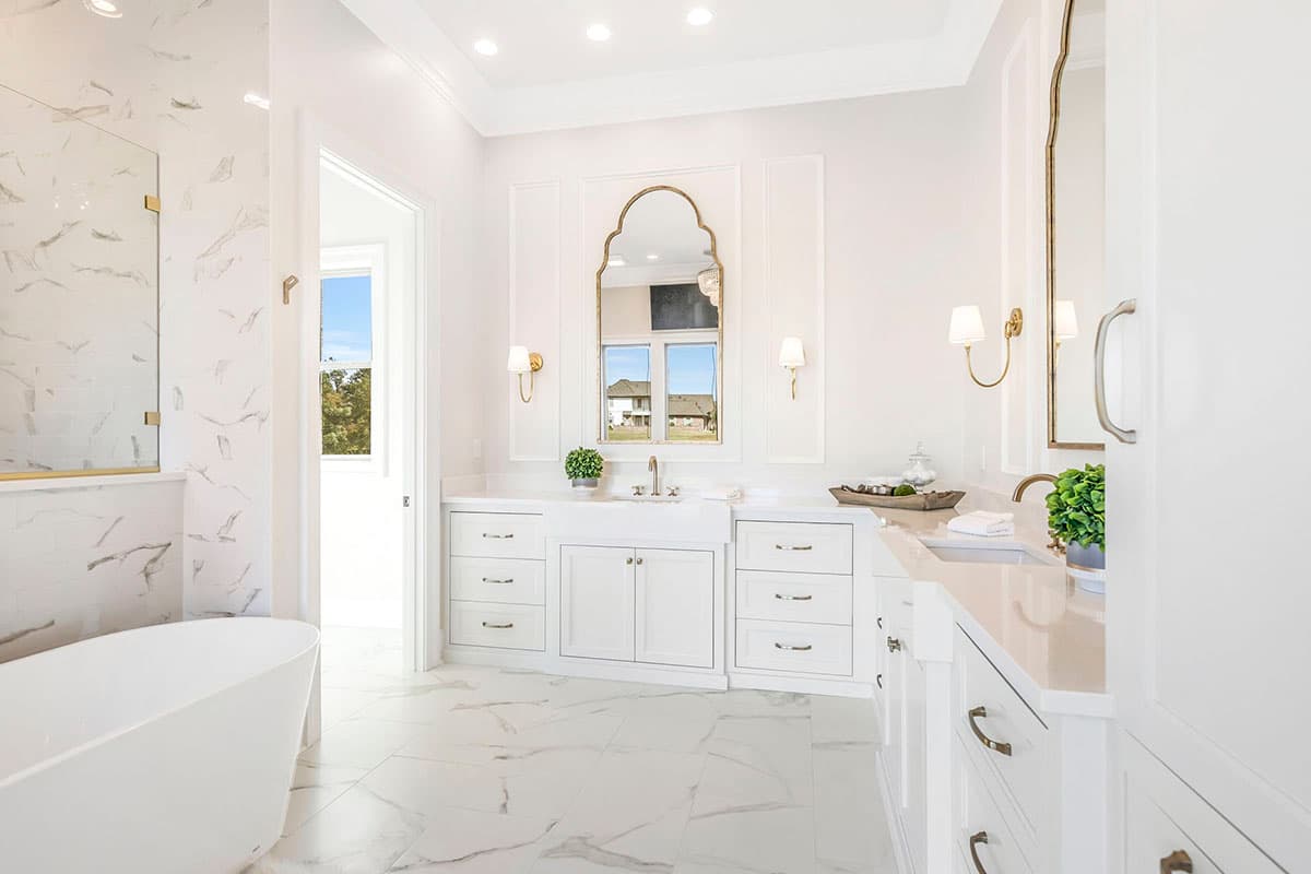Primary bathroom interior with freestanding tub, marble tile floor, custom cabinetry, and a large mirror above the sink.