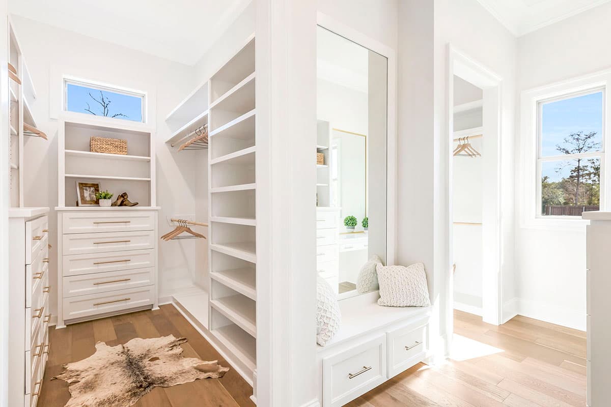 Walk-in closet interior with built-in shelving, drawers, a window, and a bench with drawers below a large mirror.