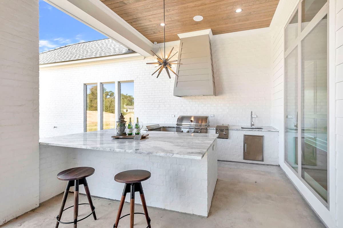 Outdoor kitchen with marble island, stainless steel appliances, and a wood-paneled ceiling. Features include a range hood and seating area.