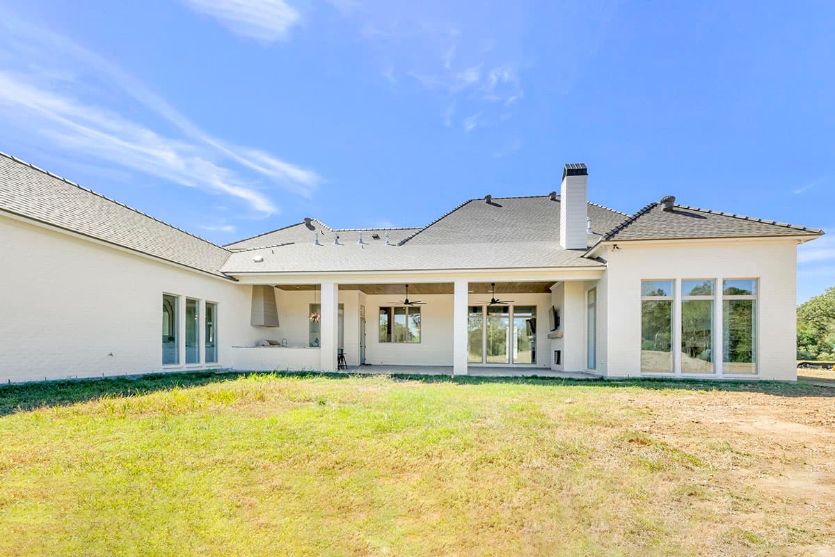 House plan exterior. One-story house with a covered porch, multiple large windows, and a chimney. White brick exterior with a dark roof.