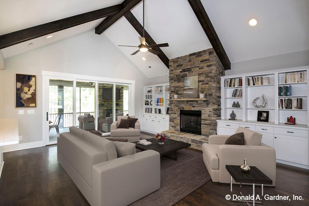 Great room with vaulted ceiling, exposed beams, stone fireplace, built-in shelving, and sliding glass doors to porch.