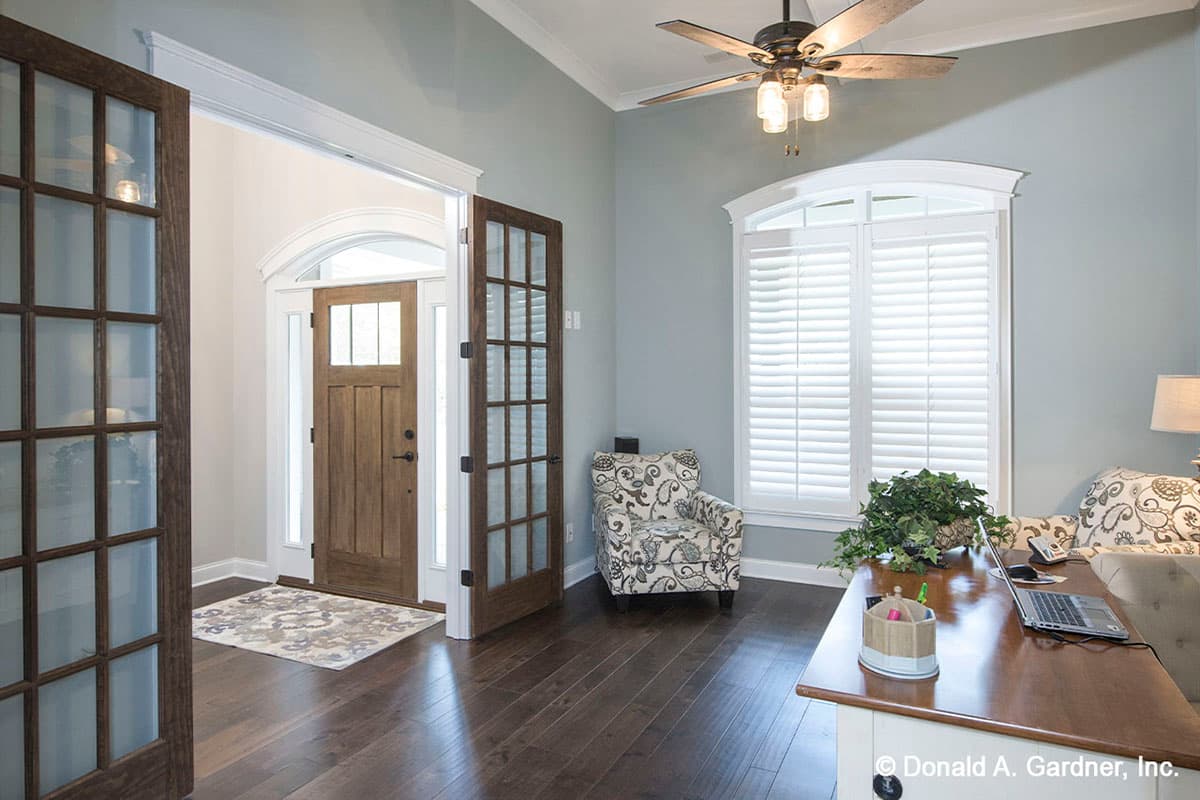 Interior view showing an entryway with wood floors, double glass doors, and a wooden front door with arched sidelights.