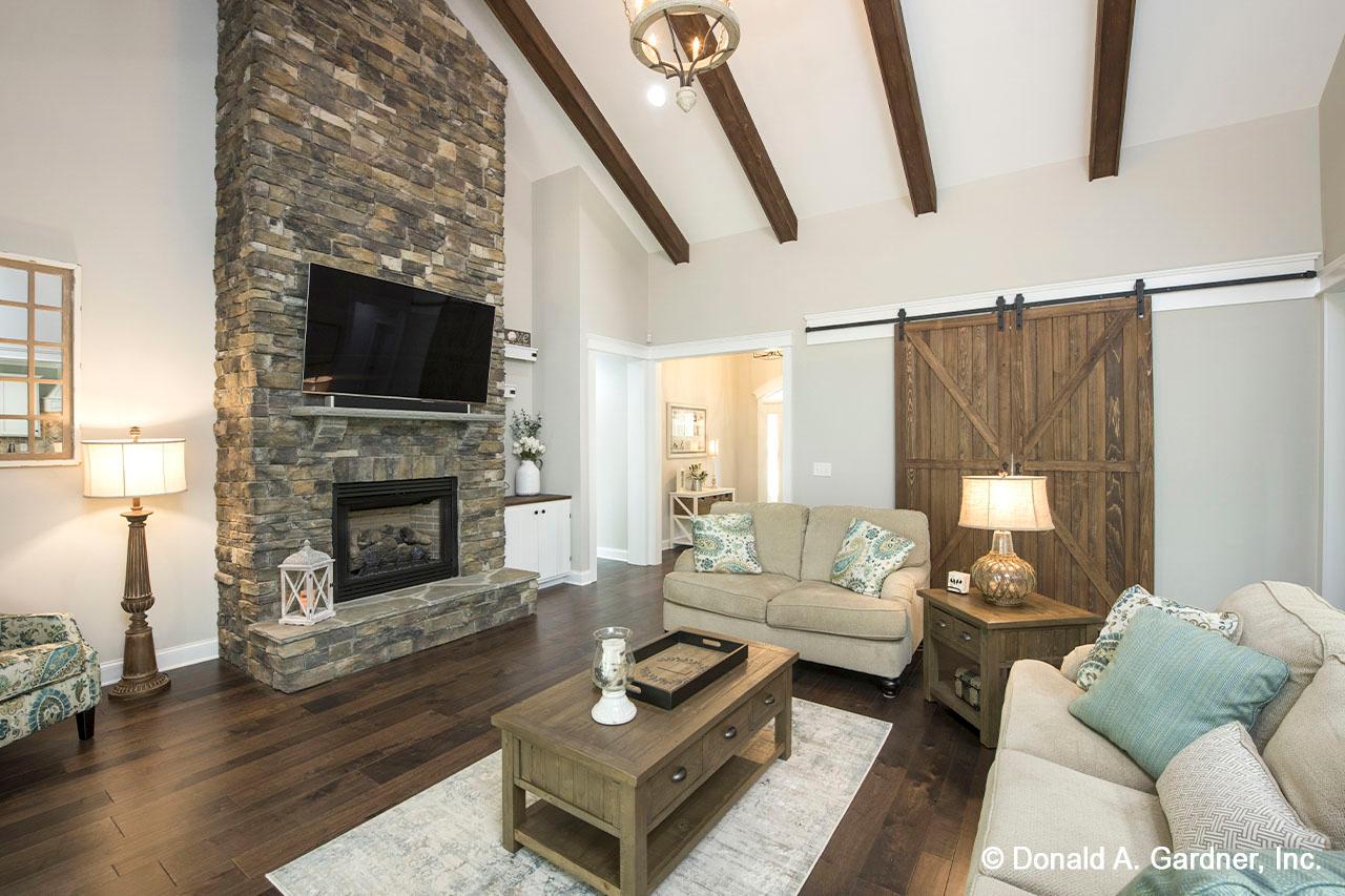 Living room with vaulted ceiling, wood beams, stone fireplace, and large wood barn door.