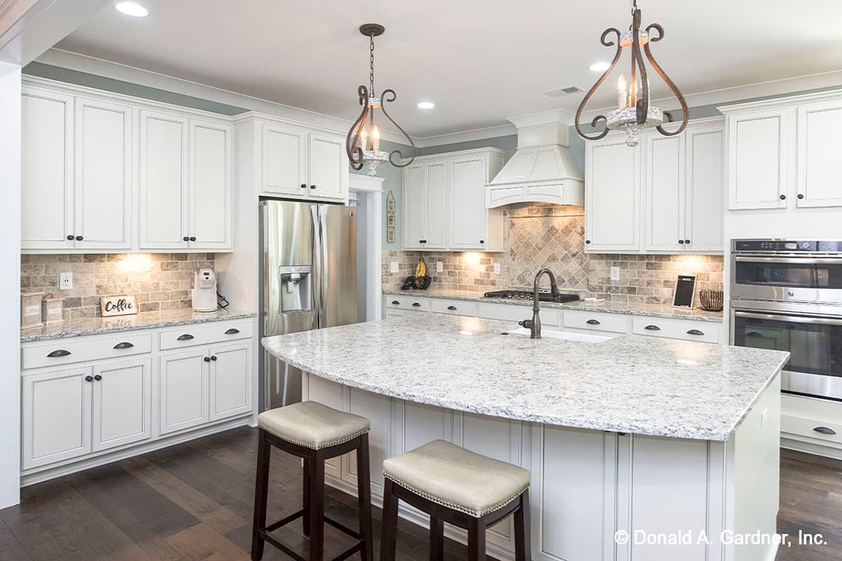 Kitchen interior with white cabinets, granite countertops, large island with seating, stainless steel appliances, and decorative pendant lights.