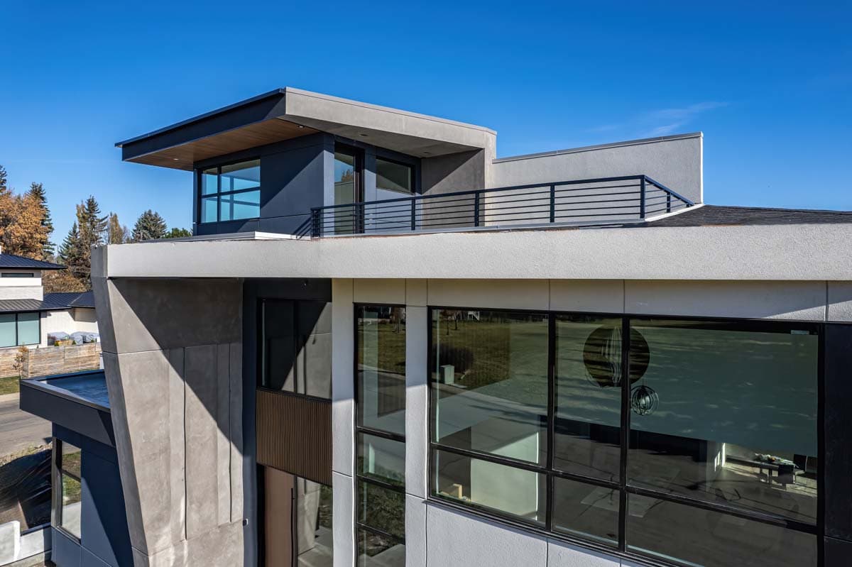 Modern house exterior with flat rooflines, cantilevered elements, extensive glazing, and a rooftop balcony.