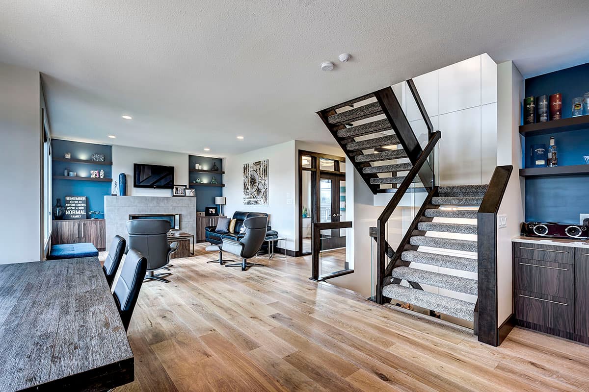 Interior view of a living room with fireplace, entertainment center, and floating staircase with glass railing.