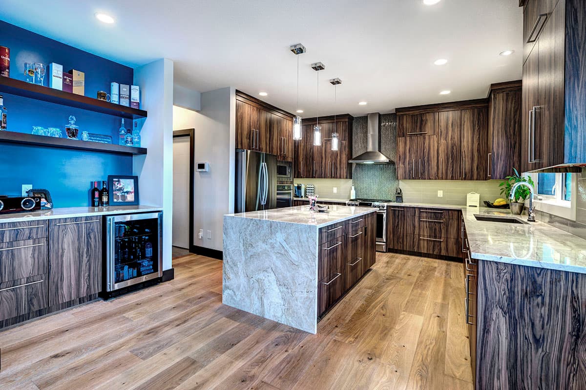 Modern kitchen with a large marble island, dark wood cabinetry, stainless steel appliances, and a built-in wine fridge.