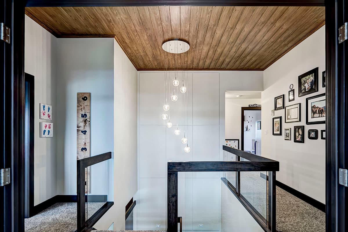 Interior view of a hallway with a wood paneled ceiling, glass railing, and a multi-bulb pendant light.