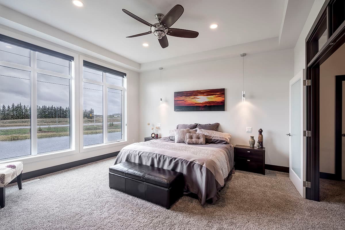 Bedroom with large windows, king-size bed, ceiling fan, and leather storage bench.