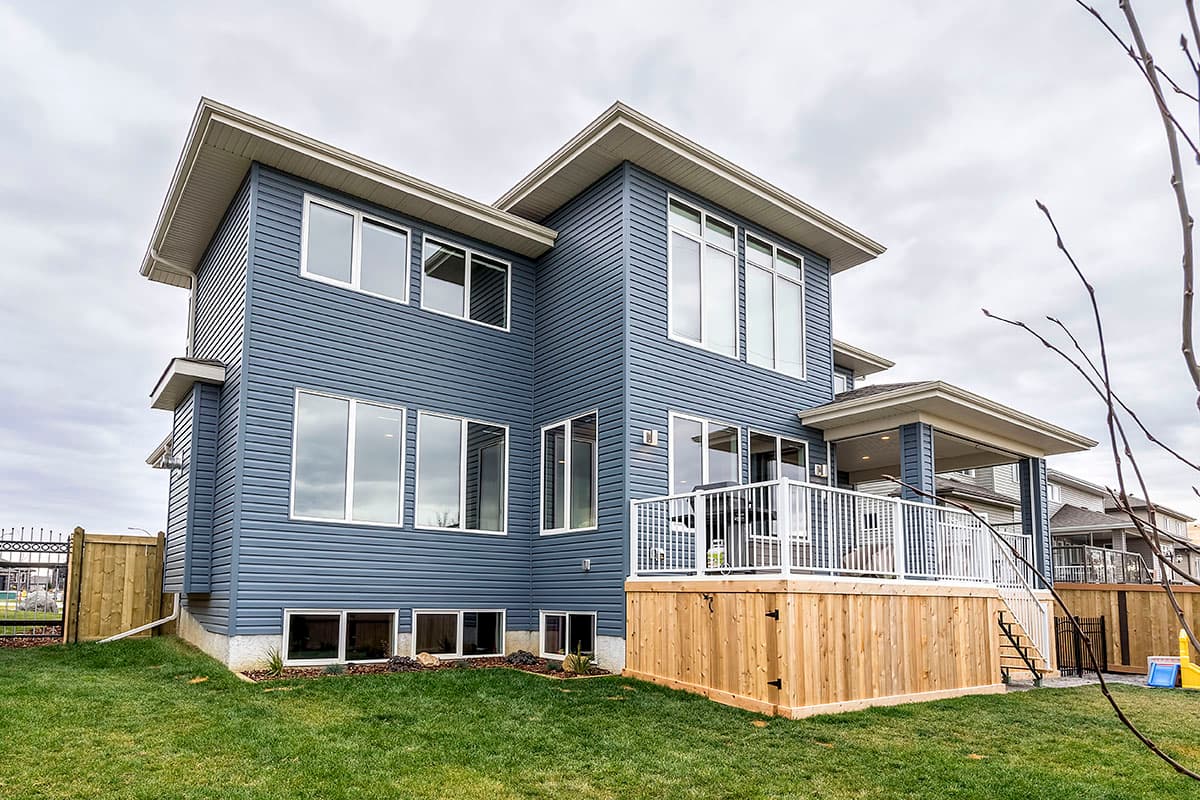 Modern house exterior plan with blue siding, multiple windows, a covered porch, and a large wooden deck with white railings.