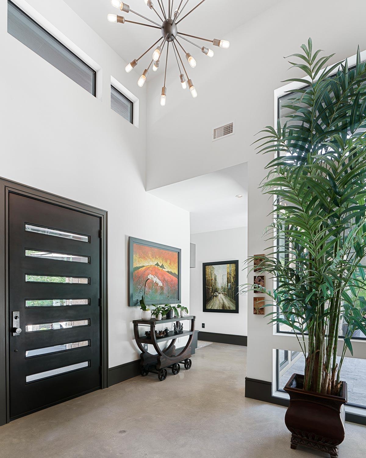 Modern entryway with glass-paneled door, high ceilings, clerestory windows, and abstract art.