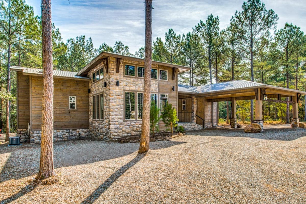 House plan exterior. Modern style with stone and wood siding. Features include a carport, flat roof, and a mix of large and small windows.