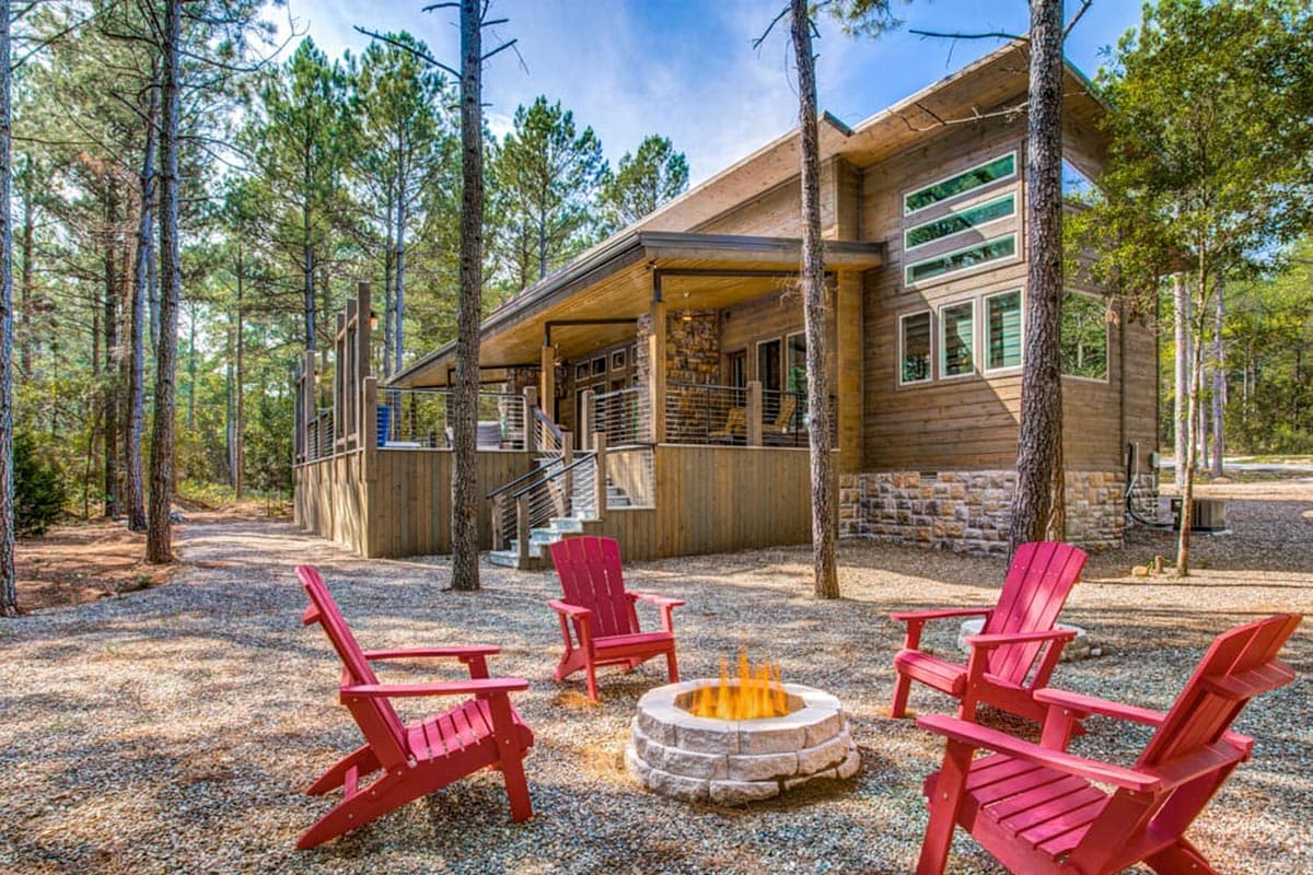 Modern cabin exterior with wood siding, stone base, wraparound deck, and horizontal windows.