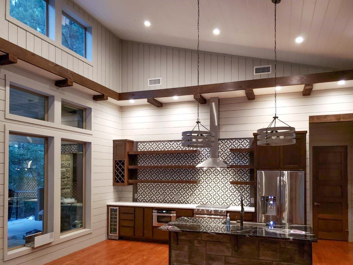 Interior view of a modern kitchen with vaulted ceilings, exposed wood beams, a large island, and a patterned tile backsplash.