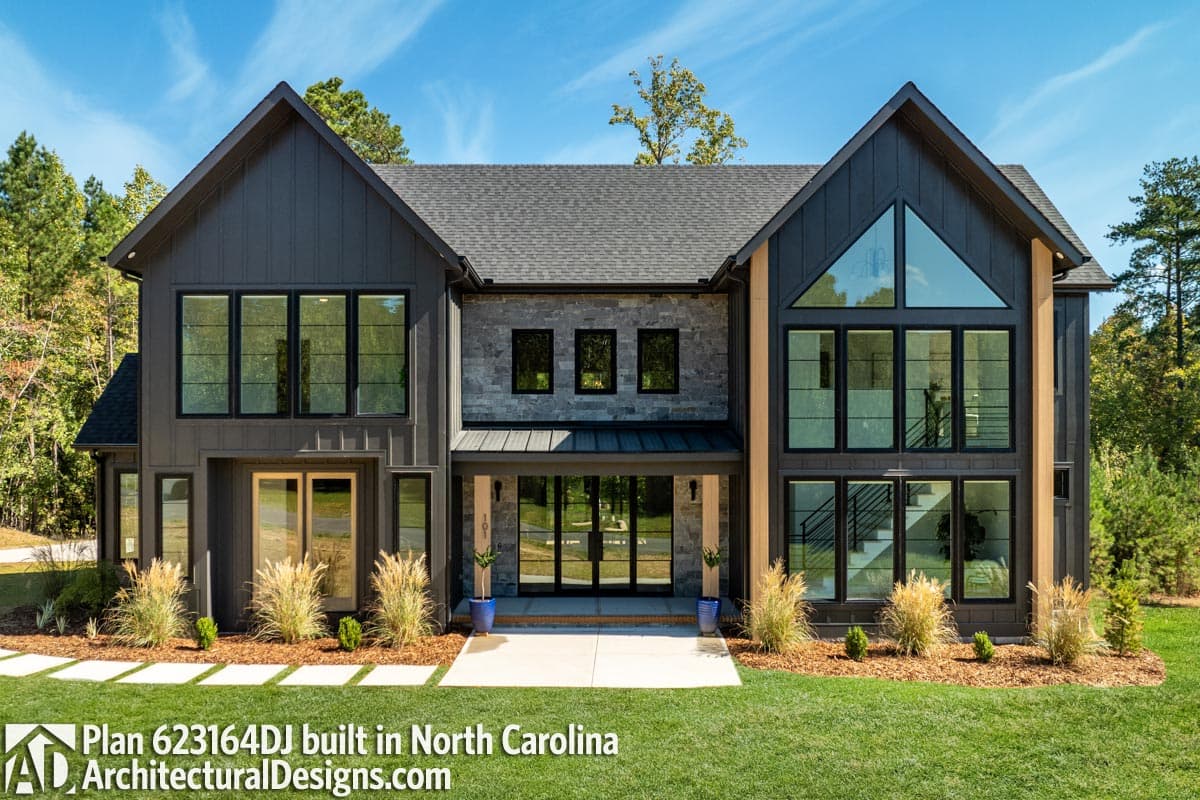 Modern Farmhouse house plan exterior with dark vertical siding, stone accents, large gables, and expansive black-framed windows.