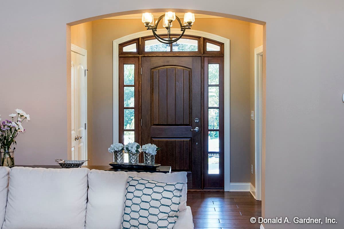 Entry hall with arched doorway, wooden door with transom windows, sidelights, and modern circular chandelier.