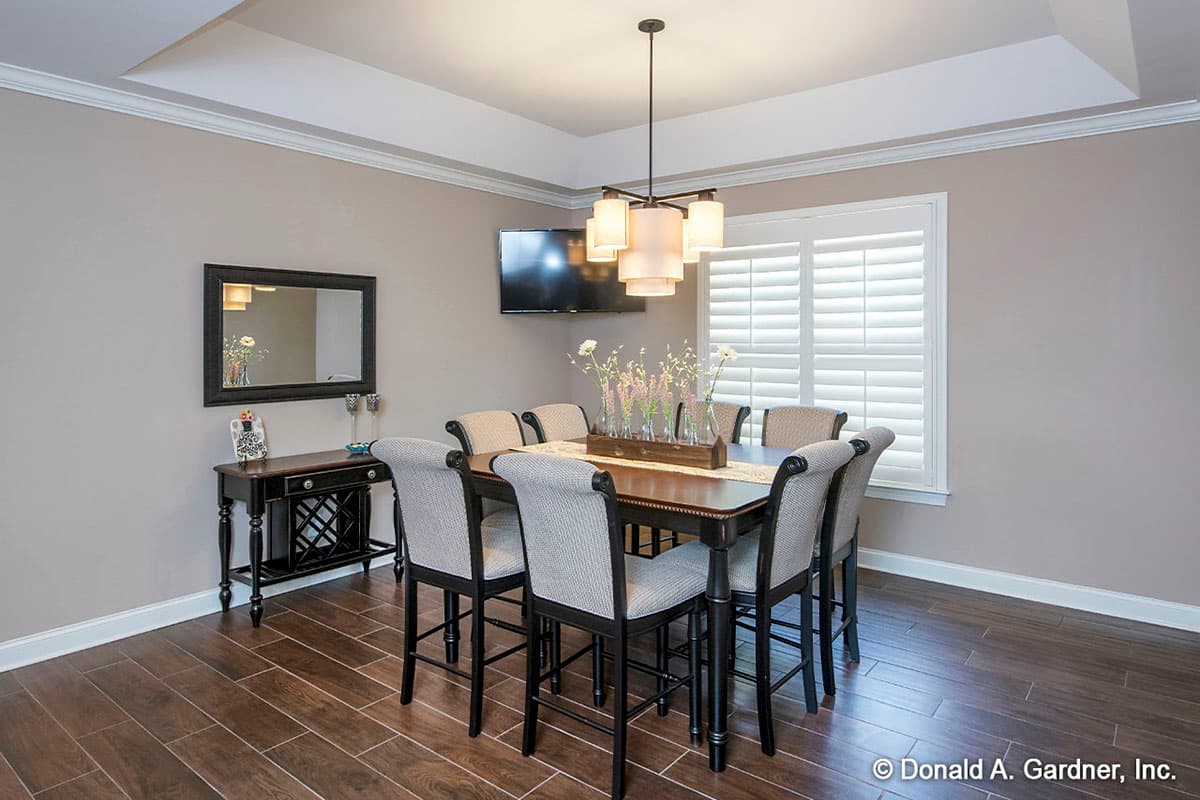 Dining room with rectangular table, eight chairs, coffered ceiling, TV, and plantation shutters.