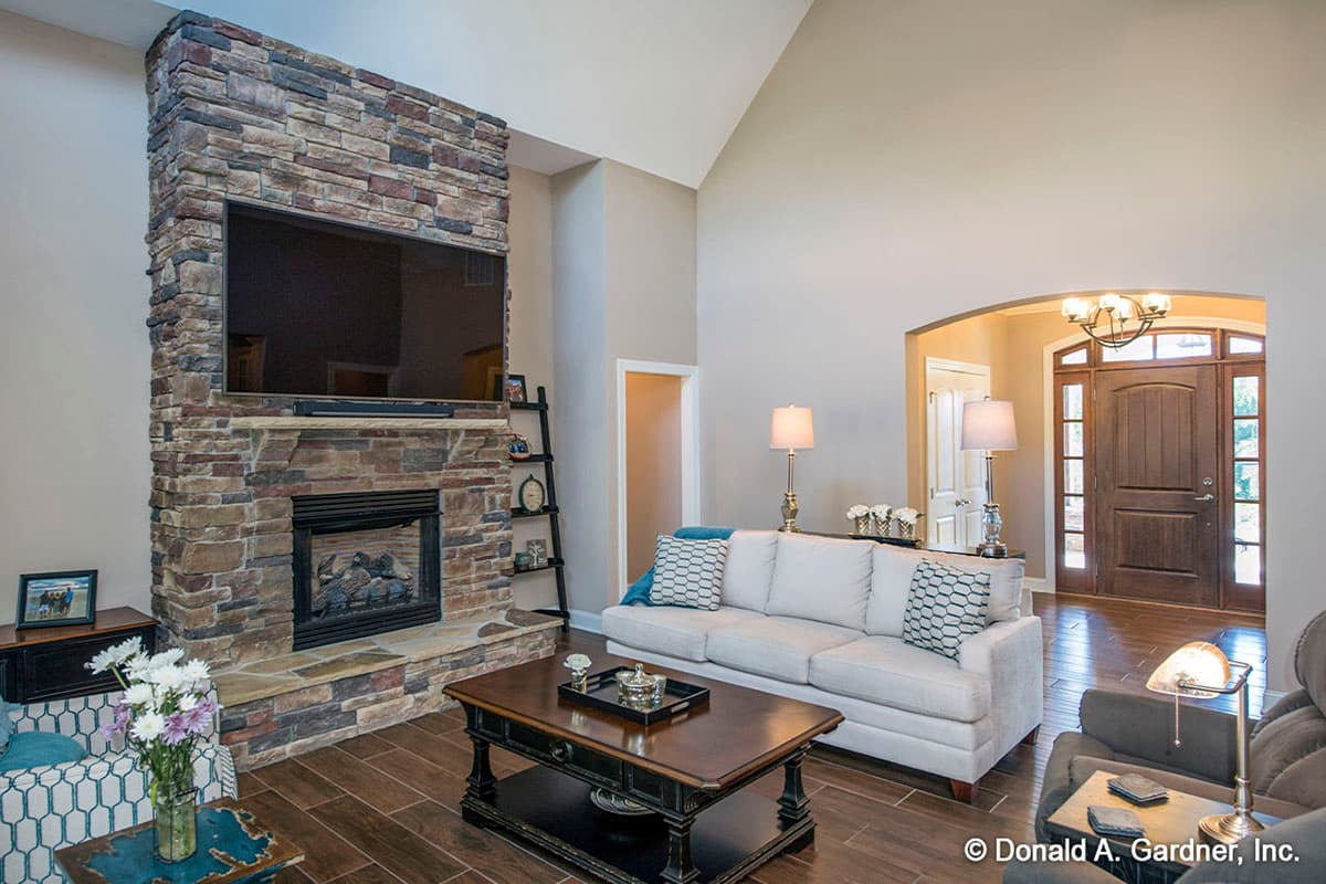 Living room with vaulted ceiling, stone fireplace, and arched entryway to front door.