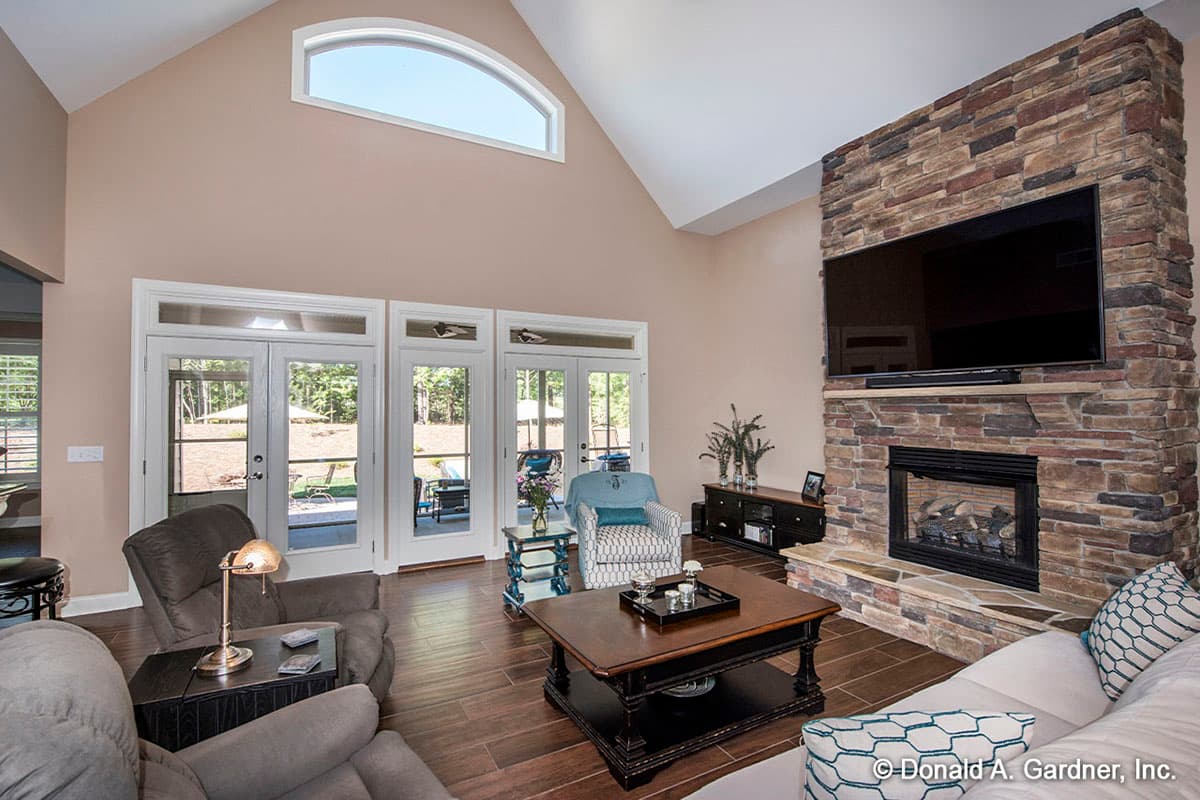 Great room with vaulted ceiling, arched transom window, stone fireplace, and French doors opening to patio.