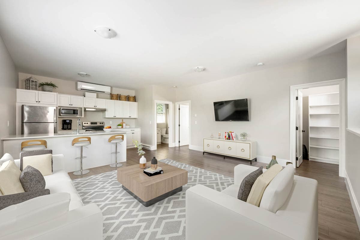 Open concept living area with kitchen island, seating for three, sofa, coffee table, and mounted television.