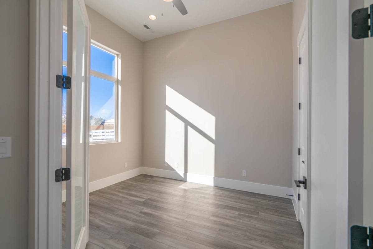 Interior view of a room with a tall window, glass-paneled door, and light gray wood-look flooring.