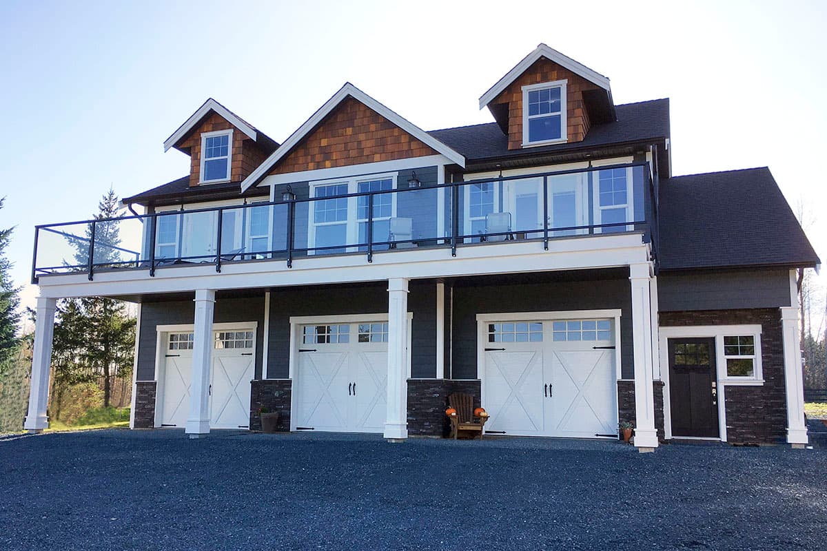 House plan exterior: Two-story Modern Farmhouse with three garage bays, deck with glass railing, and shingle accents.